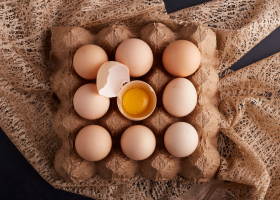 Eggs and yolk inside eggshell in the cardboard tray on a piece of burlap, top view