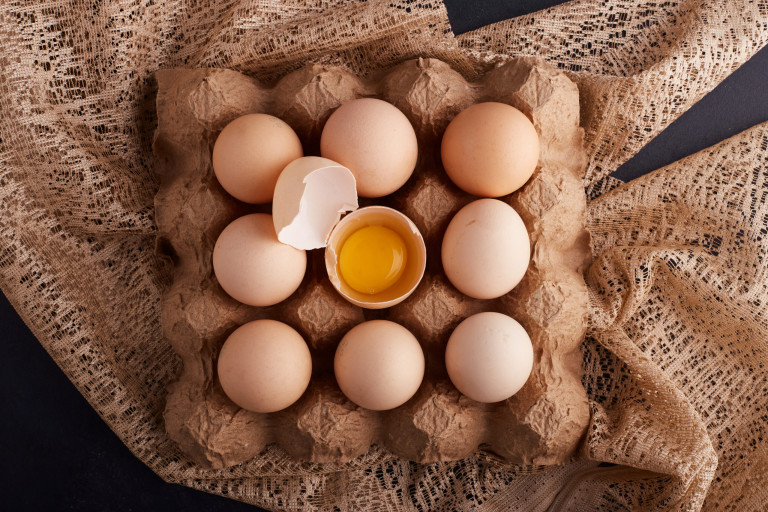 Eggs and yolk inside eggshell in the cardboard tray on a piece of burlap, top view