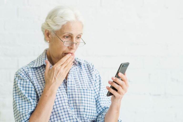 shocked-aged-woman-looking-at-mobile-against-backdrop_23-2147918183