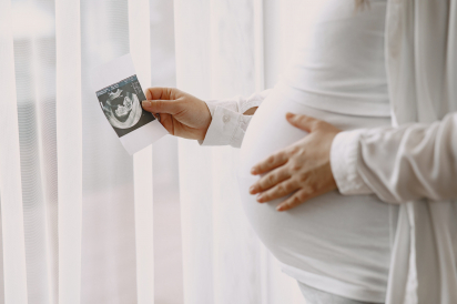 Pregnant woman stands by the window and looks at photo