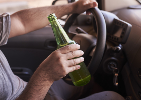 Bottle of beer in a man's hands driving the car during daytime